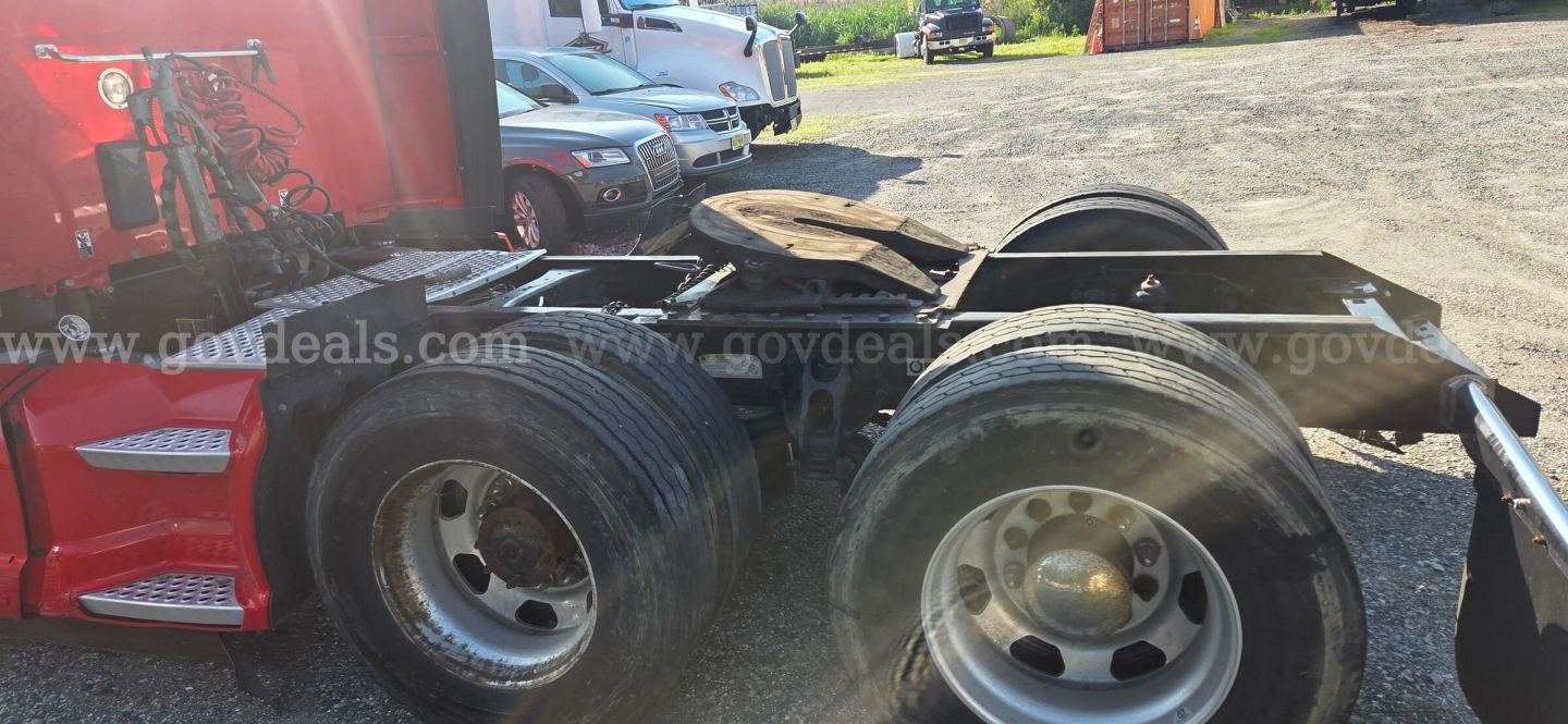 Kenworth truck chassis showing rear dual rear axles and fifth-wheel mounting with other vehicles in background.