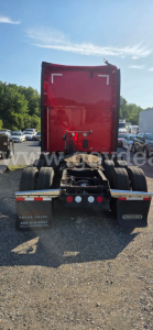 Rear view of a red Kenworth T680 tractor with fifth wheel and dual rear axles, stock plate area visible, in a lot.
