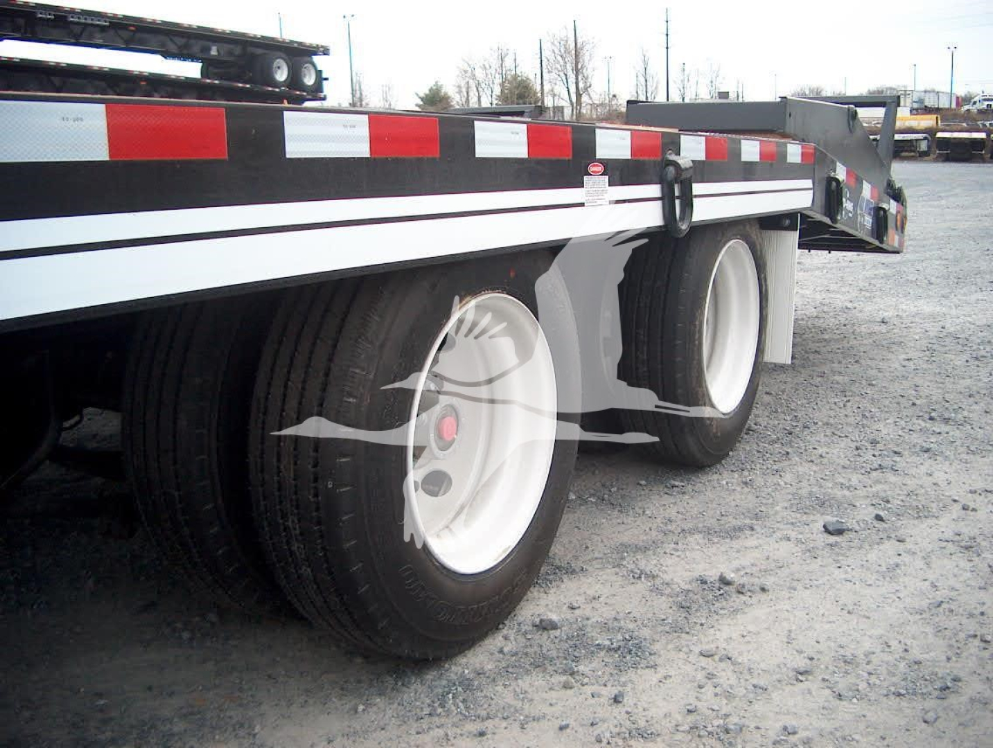 Trailer wheel area showing tandem axle and flatbed trailer with white rims and black/white striped sides.
