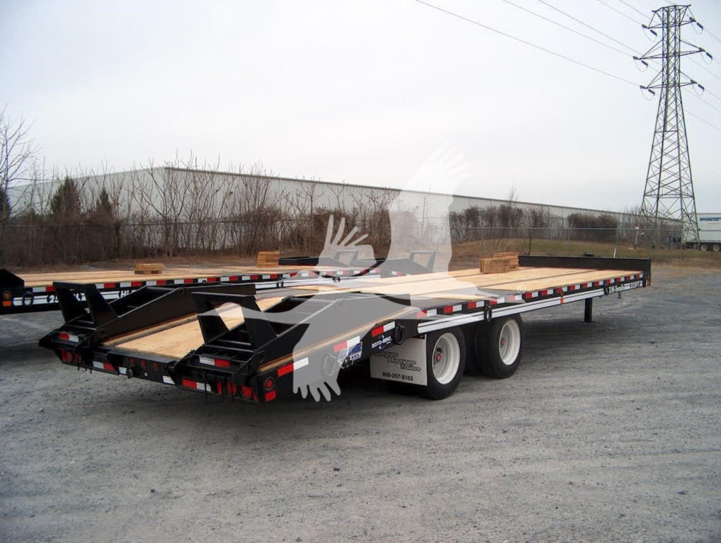 Flatbed trailer with dual rear axles and wooden deck, black frame, rear ramps folded, on gravel lot.