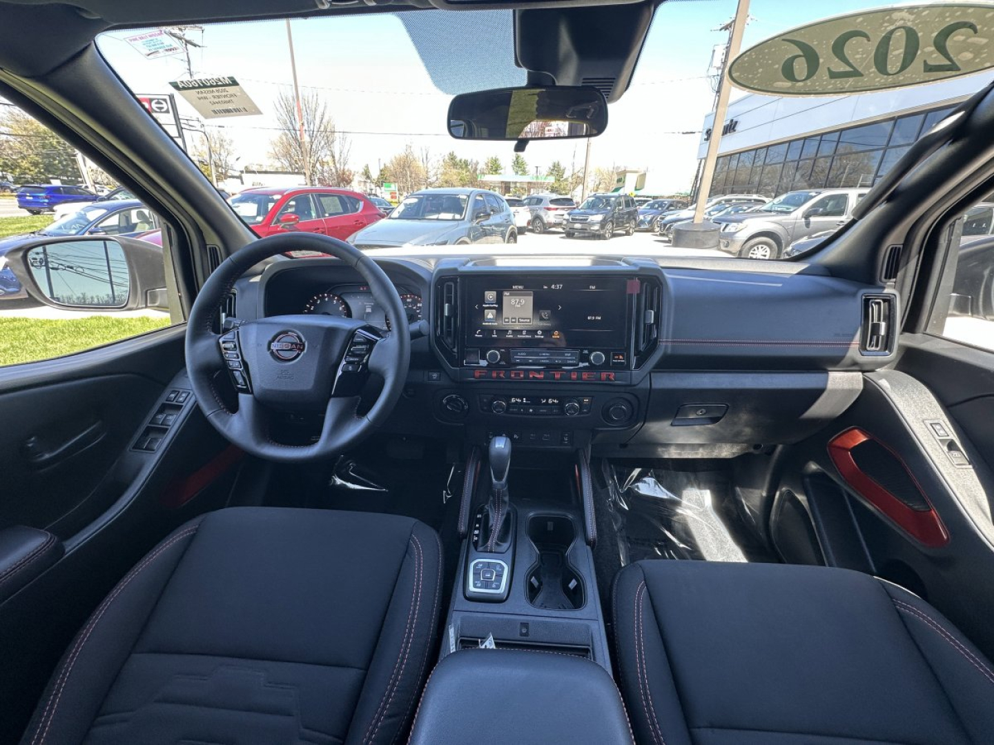Dashboard and front interior of a 2026 Nissan Frontier showing steering wheel, center stack, and gear selector in a pickup truck cabin.