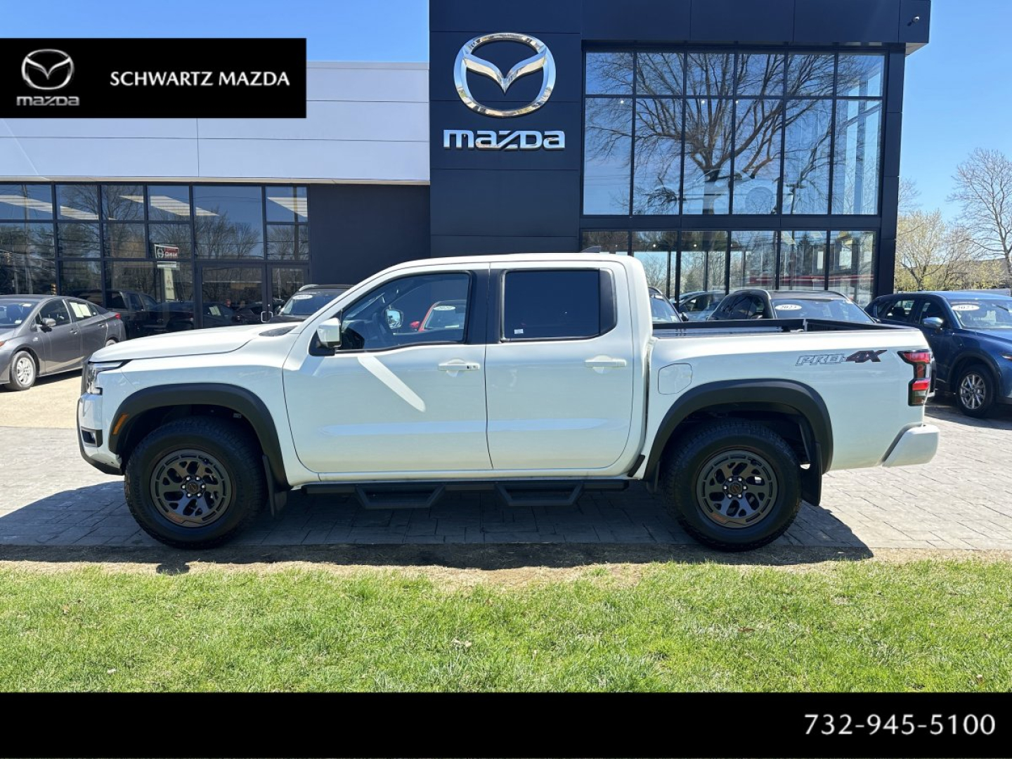 2026 Nissan Frontier pickup truck side view in front of Mazda dealership building