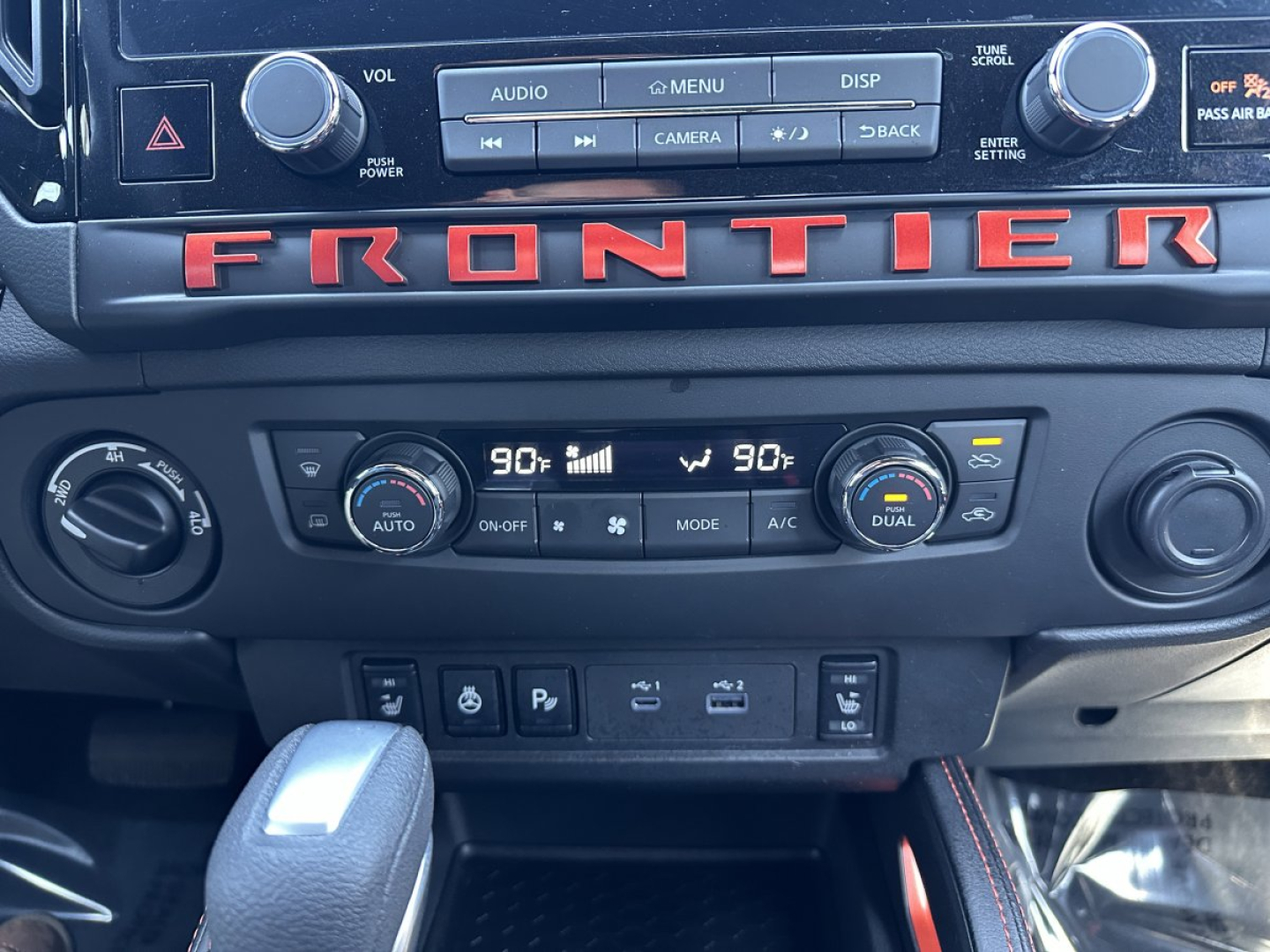 Dashboard of a Nissan Frontier interior showing dual climate controls at 90°F, prominent FRONTIER lettering across the dash, and center console controls.