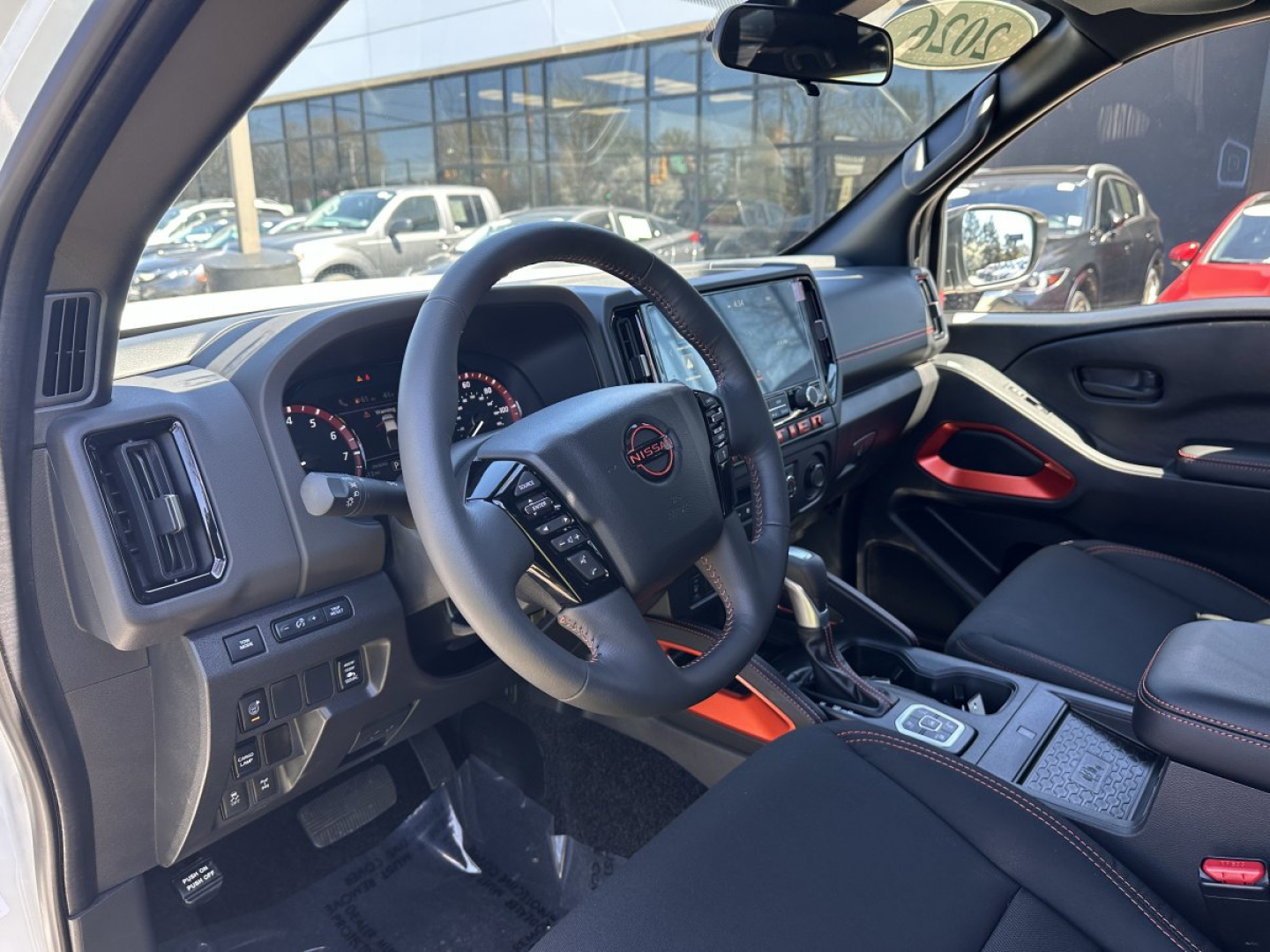 Interior of 2026 Nissan Frontier crew cab showing steering wheel, dashboard, center console, and gear selector.