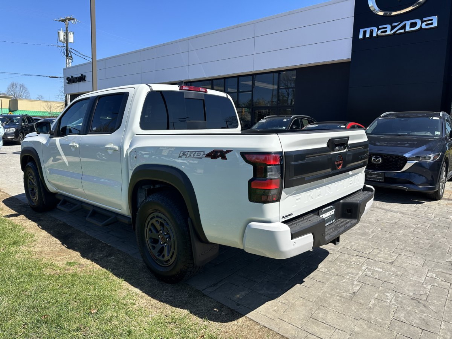 Nissan Frontier pickup truck in white, rear three-quarter view showing bed and tailgate, in a dealership lot.