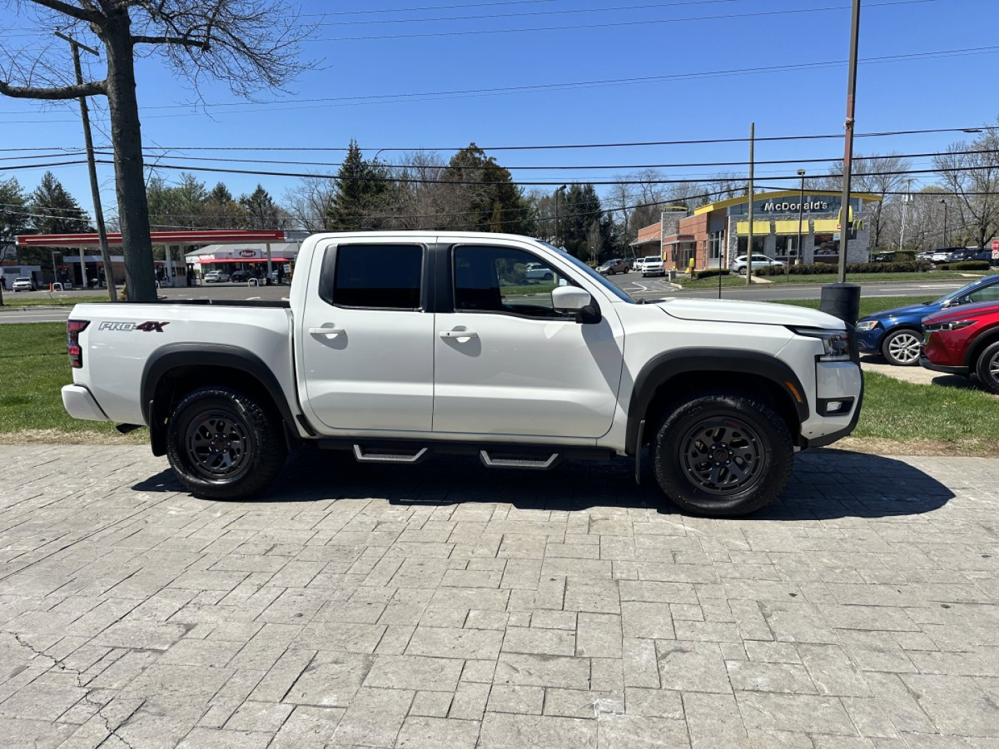 Nissan Frontier pickup truck side profile with crew cab, white color, black wheels, and 4x4 badge visible on rear body.