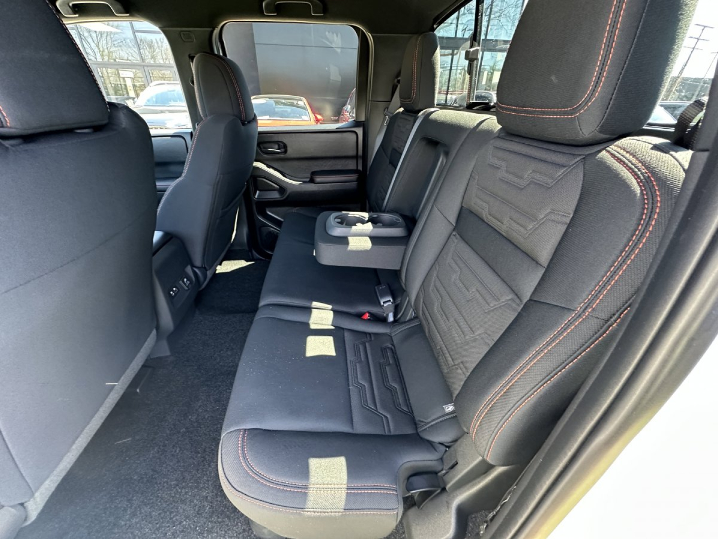 Nissan Frontier rear interior view showing black cloth seats with red contrast stitching and center armrest; spacious back row.