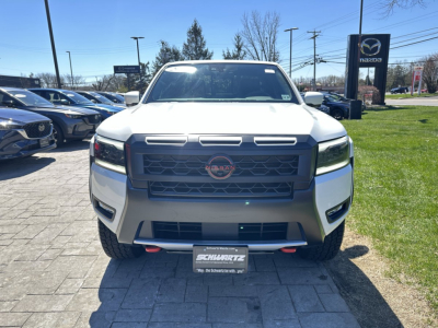 Front view of a white 2026 Nissan Frontier pickup truck in a dealership lot with Nissan badge on grille and black stock bumper; visible front license plate frame from Schwarcz.