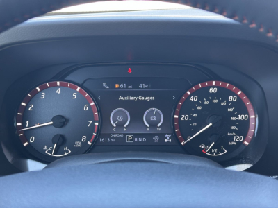 Dashboard of a 2026 Nissan Frontier showing instrument cluster with speedometer, tachometer, and center display reading Auxiliary Gauges and gear selector PRND; mileage 1613 mi.
