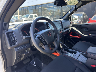 Interior of 2026 Nissan Frontier crew cab showing steering wheel, dashboard, center console, and gear selector.