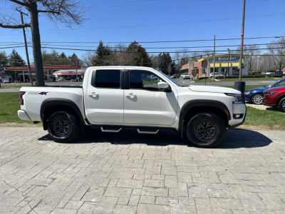 Nissan Frontier pickup truck side profile with crew cab, white color, black wheels, and 4x4 badge visible on rear body.