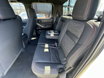Nissan Frontier rear interior view showing black cloth seats with red contrast stitching and center armrest; spacious back row.