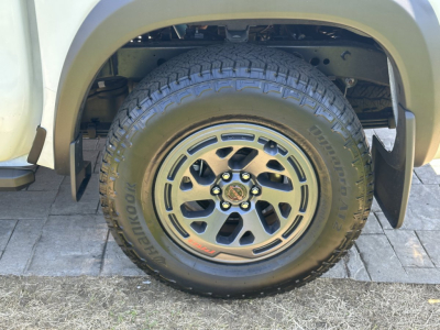 Front right wheel well of a pickup truck with a Goodyear Wrangler tire mounted on a black and gray alloy wheel; tire tread visible, wheel bolts center cap.