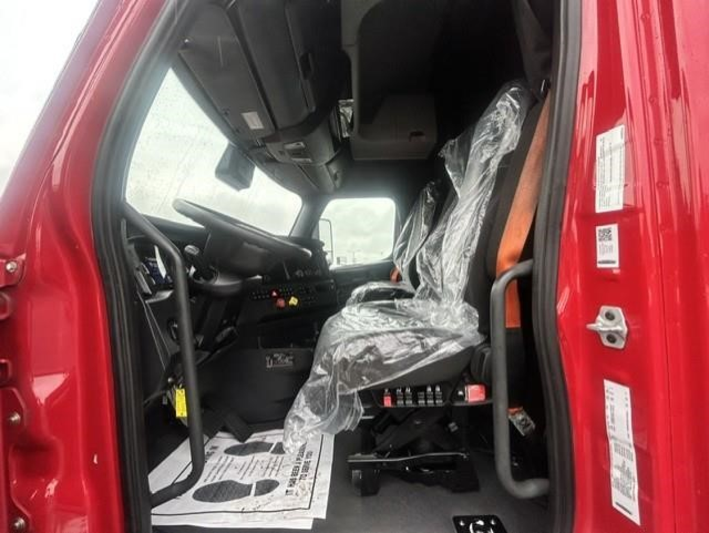 Truck cab interior of a 2023 Freightliner Cascadia showing driver seat with plastic cover and dashboard controls.