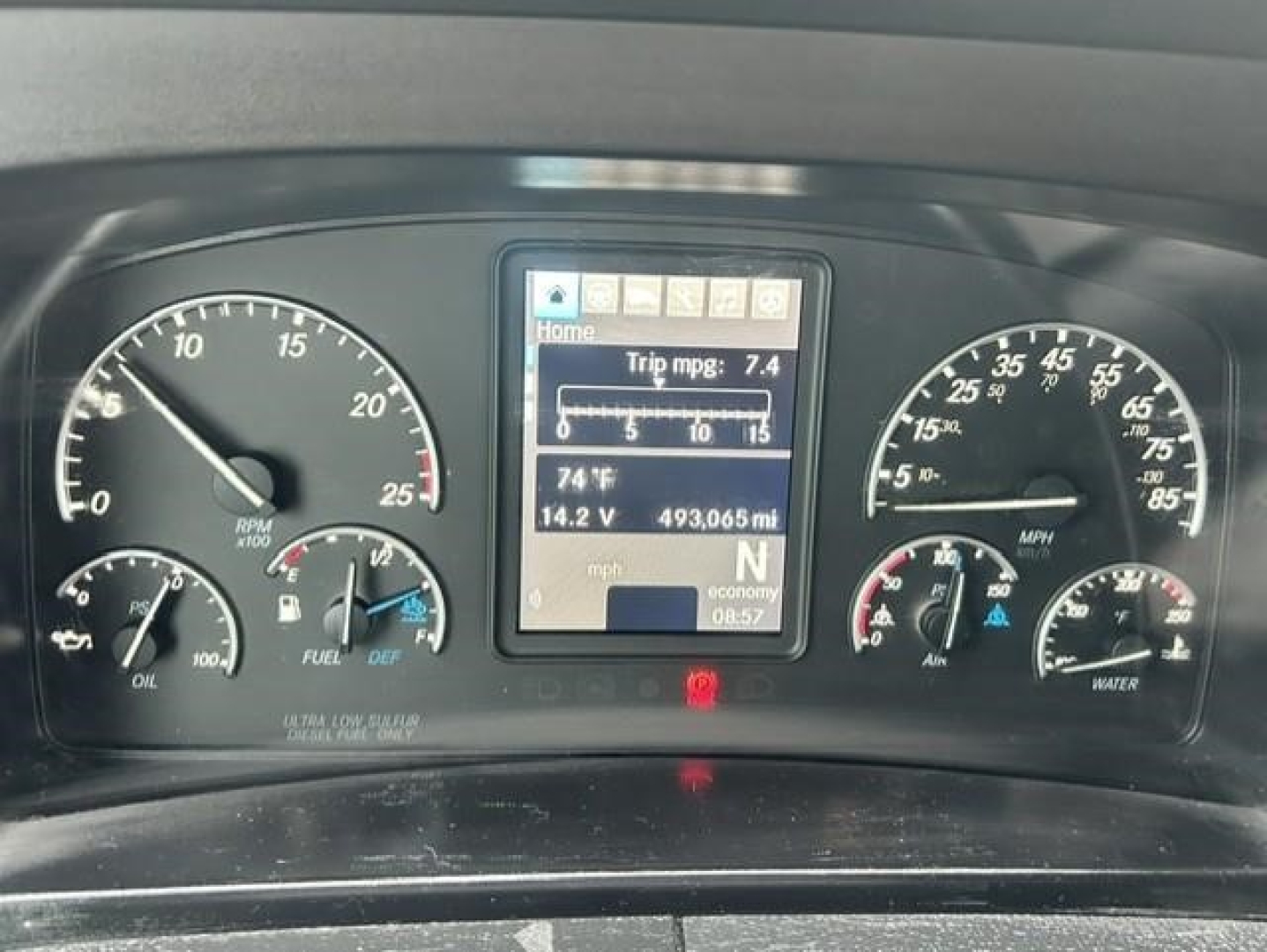 Dashboard of a Freightliner Cascadia showing gauges, center display with trip mpg 7.4 and 493.065 mi distance.