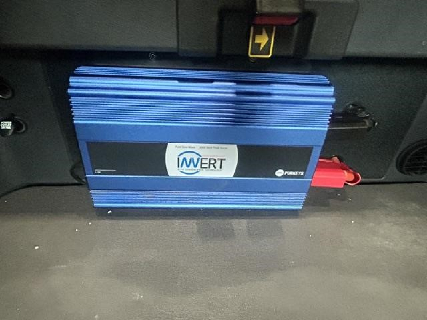 Blue IMWERT device mounted under dashboard of Freightliner Cascadia cab, with red connector plugged in, front view showing sticker and cooling fins.