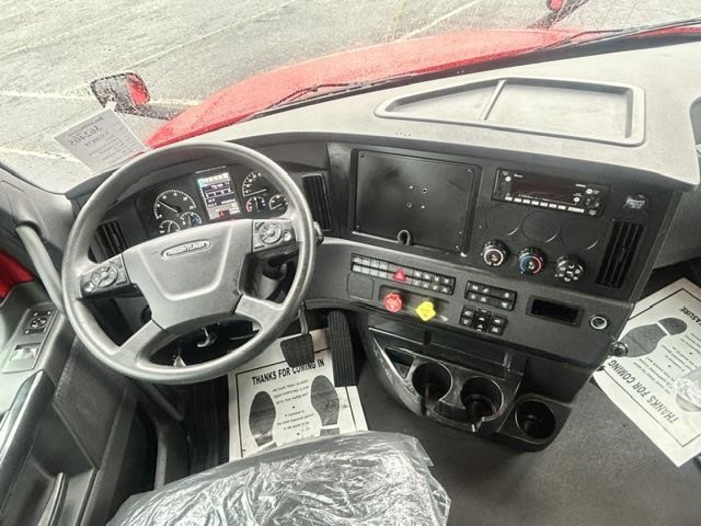 Cab interior of a Freightliner Cascadia truck showing steering wheel, dashboard with gauges, center console, and multiple control panels.