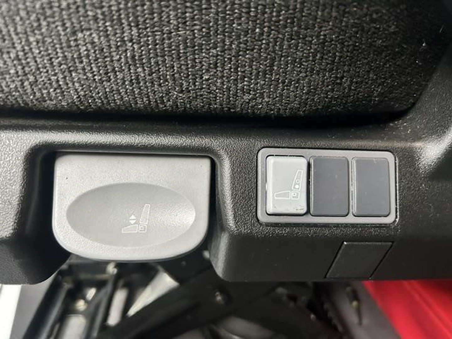 Seat heater or lumbar control panel with three small blank buttons and a larger rounded switch labeled with a seat icon, located on a truck interior panel.