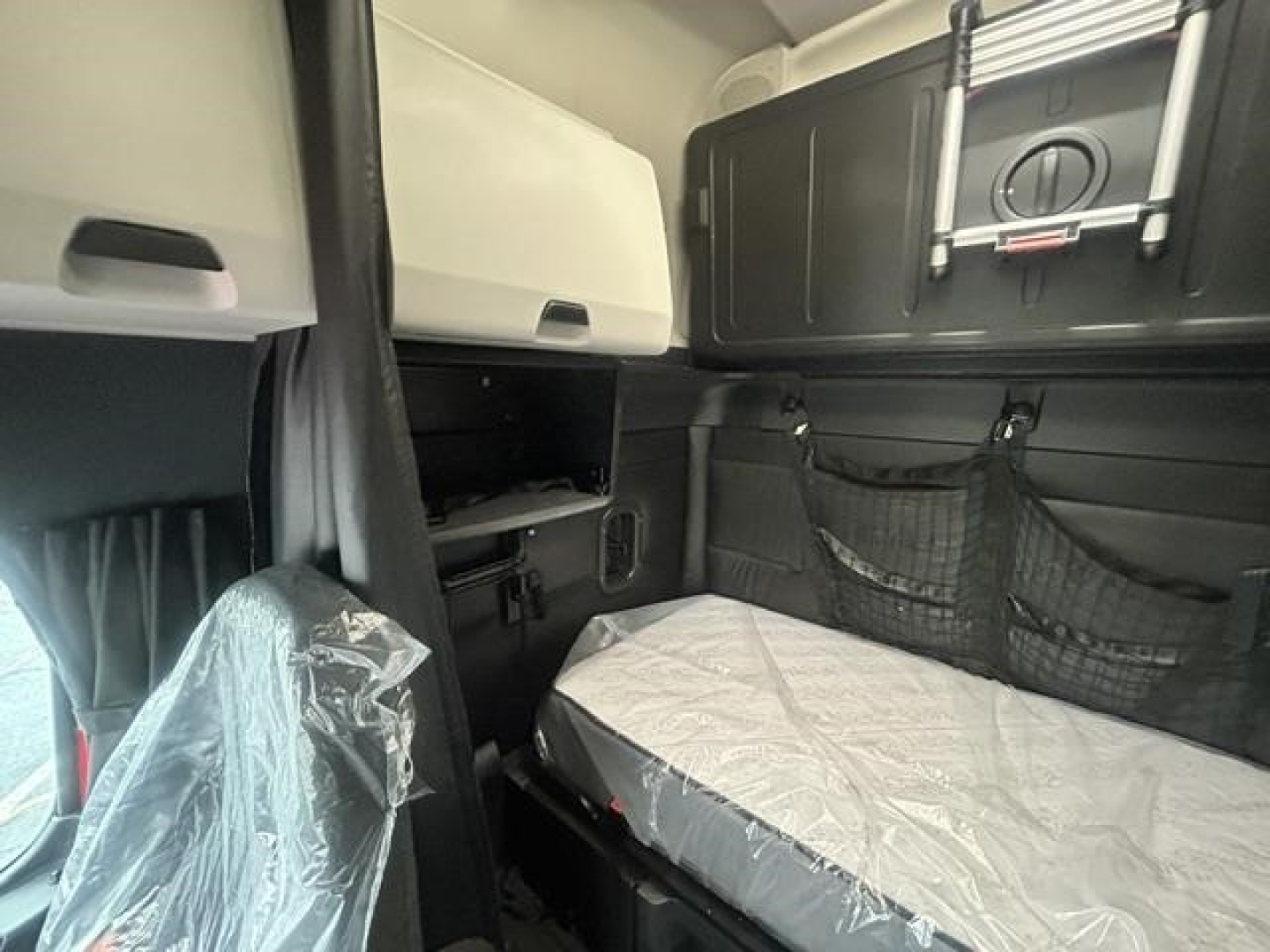 Interior of a Freightliner Cascadia truck sleeper cab with bunk bed area and storage compartments visible.