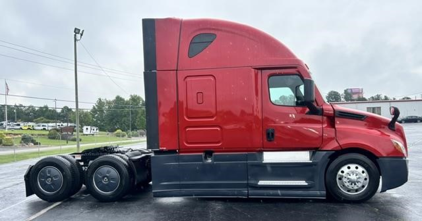 Truck side view showing a red Freightliner Cascadia tractor with sleeper cabin and multiple rear axles.