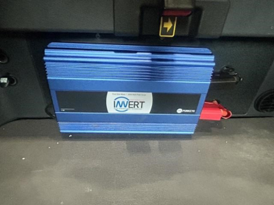 Blue IMWERT device mounted under dashboard of Freightliner Cascadia cab, with red connector plugged in, front view showing sticker and cooling fins.