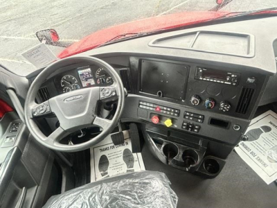 Cab interior of a Freightliner Cascadia truck showing steering wheel, dashboard with gauges, center console, and multiple control panels.