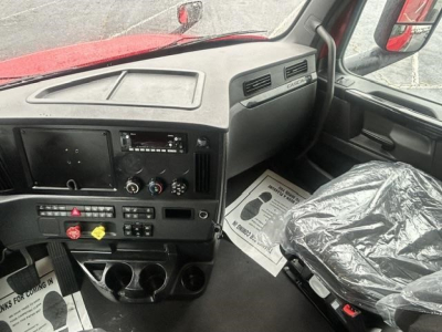 Cab interior of a Freightliner Cascadia truck showing dashboard with controls, steering area, and driver seat covered in plastic.