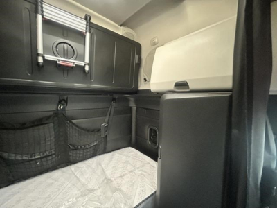 Cab interior of a Freightliner Cascadia sleeper showing storage nets, a small cabinet, and a bed platform.
