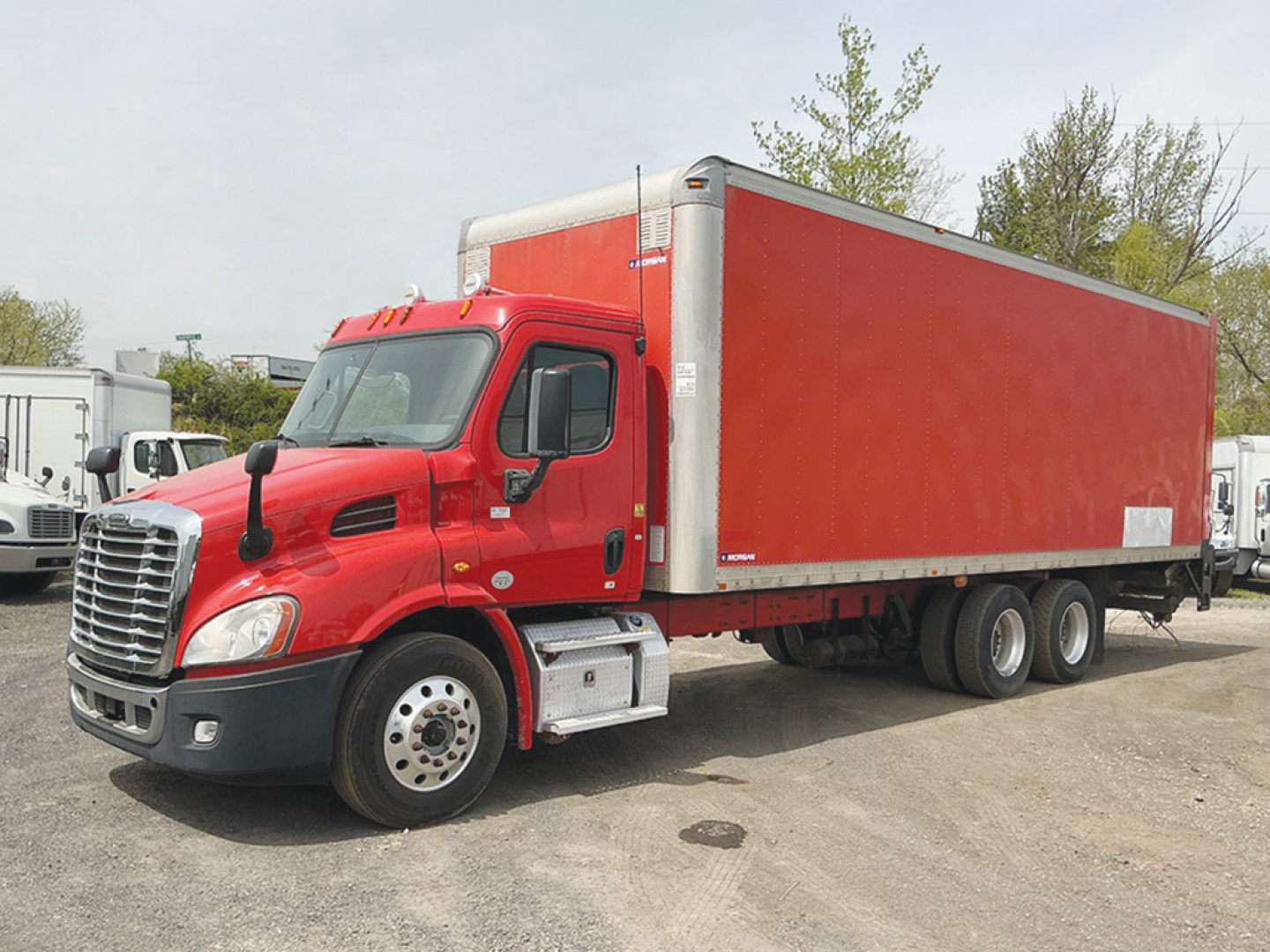 Freightliner Cascadia113 conventional daycab truck with red cab and long red cargo box, side view.