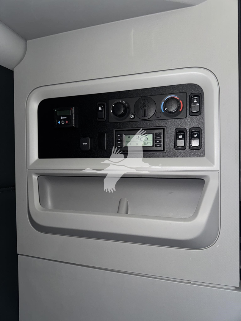 Kenworth T680 dash cluster and controls with climate knobs, radio, and storage compartment.