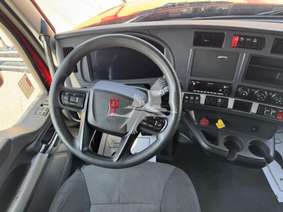 Cockpit of a 2023 Kenworth T680 truck showing steering wheel with Kenworth emblem, dashboard controls, gauges, and gear shifter.