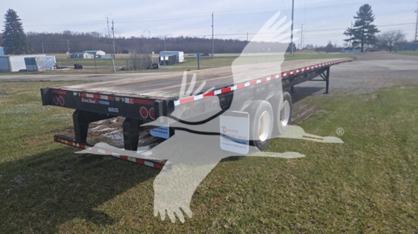 Great Dane steel flatbed trailer showing long flatbed with dual rear axles and red/white reflective safety tape. Visible text or labels not legible.