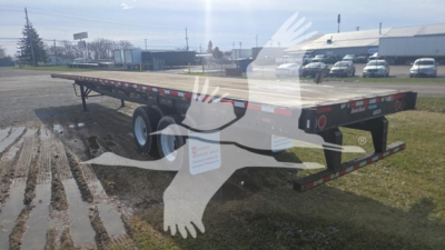 Great Dane flatbed trailer showing steel deck and dual axles with reflective red and white tape and bumper at rear.