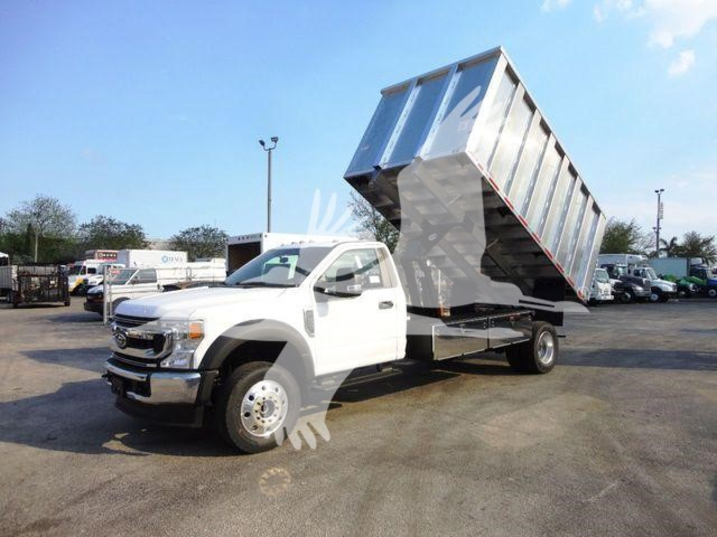 Ford F-600 dump truck with raised silver dump bed in a dealership lot.