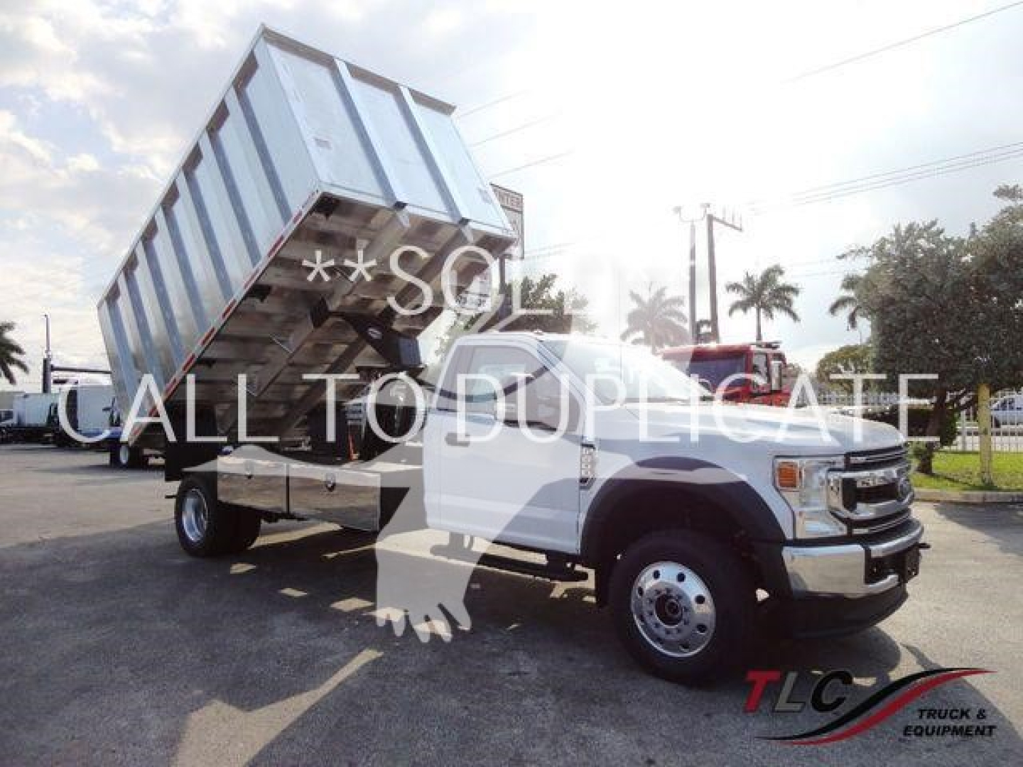 Dump truck in raised bed position showing cargo bed on a Ford F-Series chassis with chipper truck branding faintly visible.