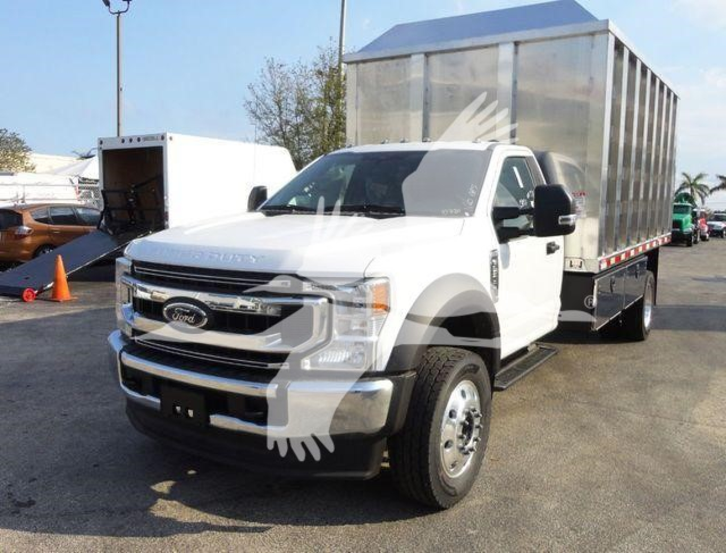Ford F-600 truck with flatbed and cargo trailer parked, front-left view showing white cab and silver chassis, chipper truck body in background.