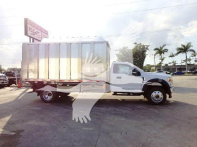Ford F-600 medium-duty truck with a large metallic dump bed/trailer cargo area in a dealership lot, side view, white cab and gray metallic body.