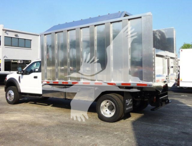 Ford F-600 dump/chipper truck side view showing large metallic dump body with reflective panels and white cab.