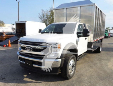 Ford F-600 truck with flatbed and cargo trailer parked, front-left view showing white cab and silver chassis, chipper truck body in background.