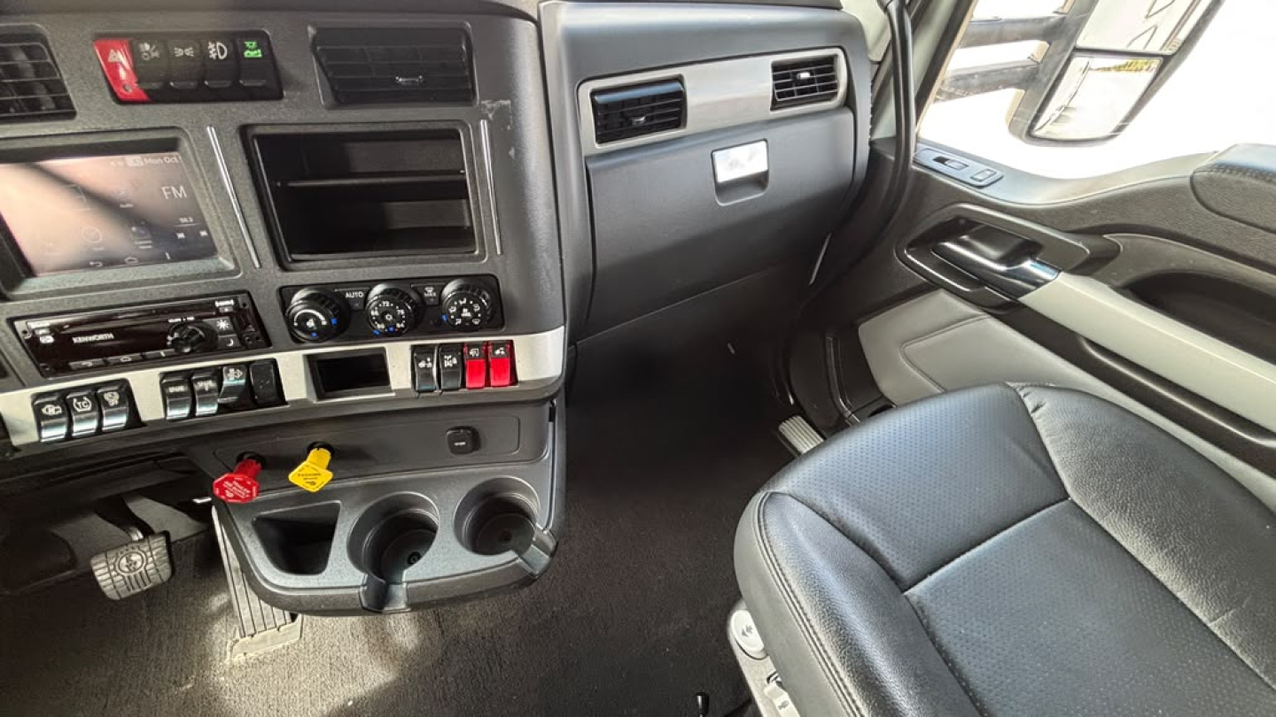 Kenworth T680 cab interior dash and driver seat with center console and cup holders.
