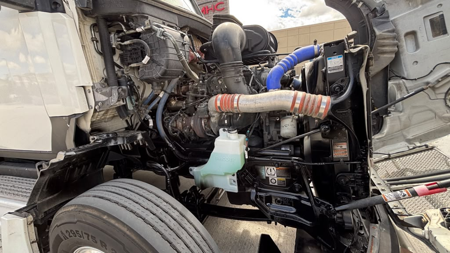Kenworth T680 engine bay showing coolant reservoir and intake hoses with exposed engine components.