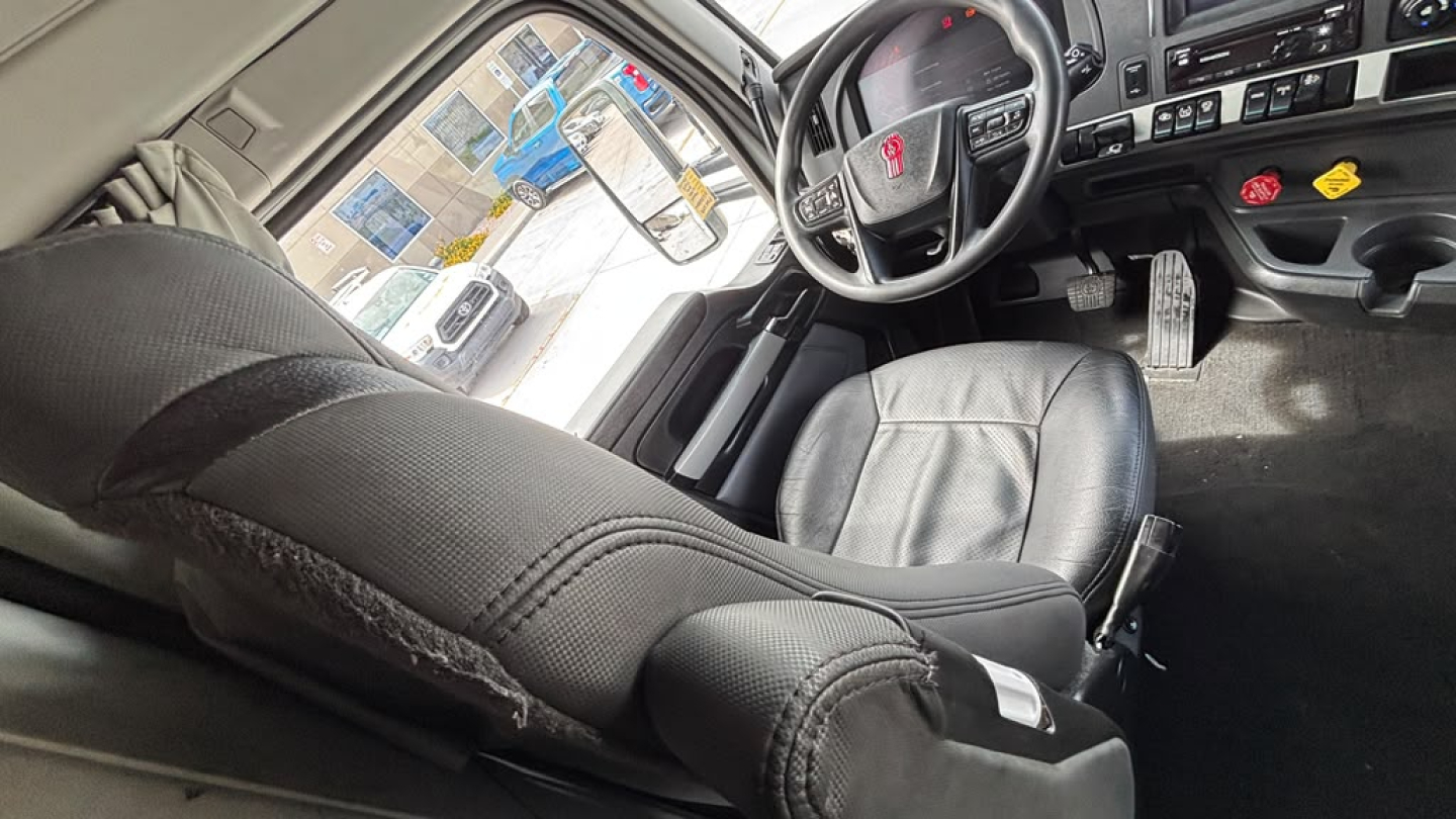 Kenworth T680 truck interior with steering wheel, driver seat, and dashboard visible; worn fabric on armrest and pedals seen.
