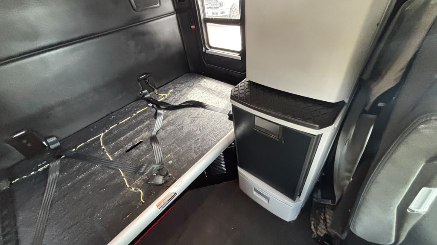 Kenworth T680 interior cargo area with seating and storage unit in view showing black interior and seat belt anchor.