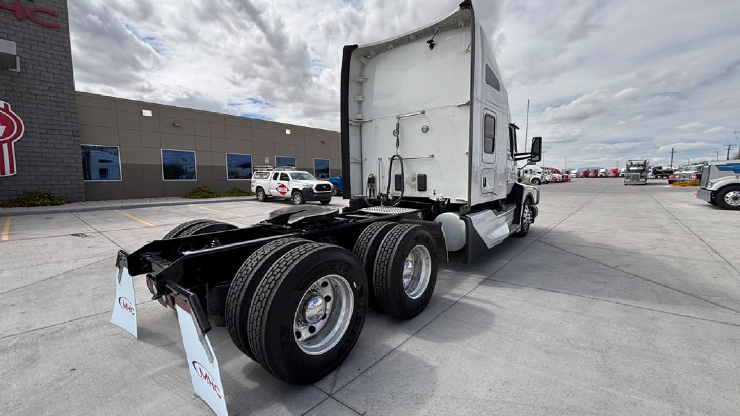 Kenworth T680 tractor trailer in a parking lot showing rear triple-axle configuration and white cab.