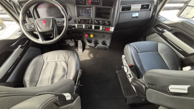 Kenworth T680 cab interior showing steering wheel, dashboard, and driver seats in a sleeper truck.