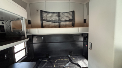 Interior sleeper cab of a Kenworth truck with side storage cabinets and a cargo net at the back wall. No visible branding text beyond the truck's interior features.