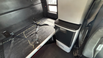 Kenworth T680 interior cargo area with seating and storage unit in view showing black interior and seat belt anchor.