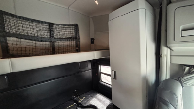 Truck cab interior of a 2023 Kenworth T680 showing sleeper bunk area and storage cabinet with window