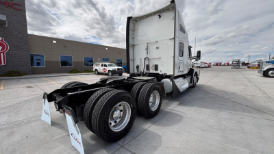 Kenworth T680 tractor trailer in a parking lot showing rear triple-axle configuration and white cab.