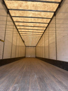 Interior of a 2016 Wabash van trailer with wooden flooring and ribbed ceiling, empty cargo space, side walls, rear end visible.